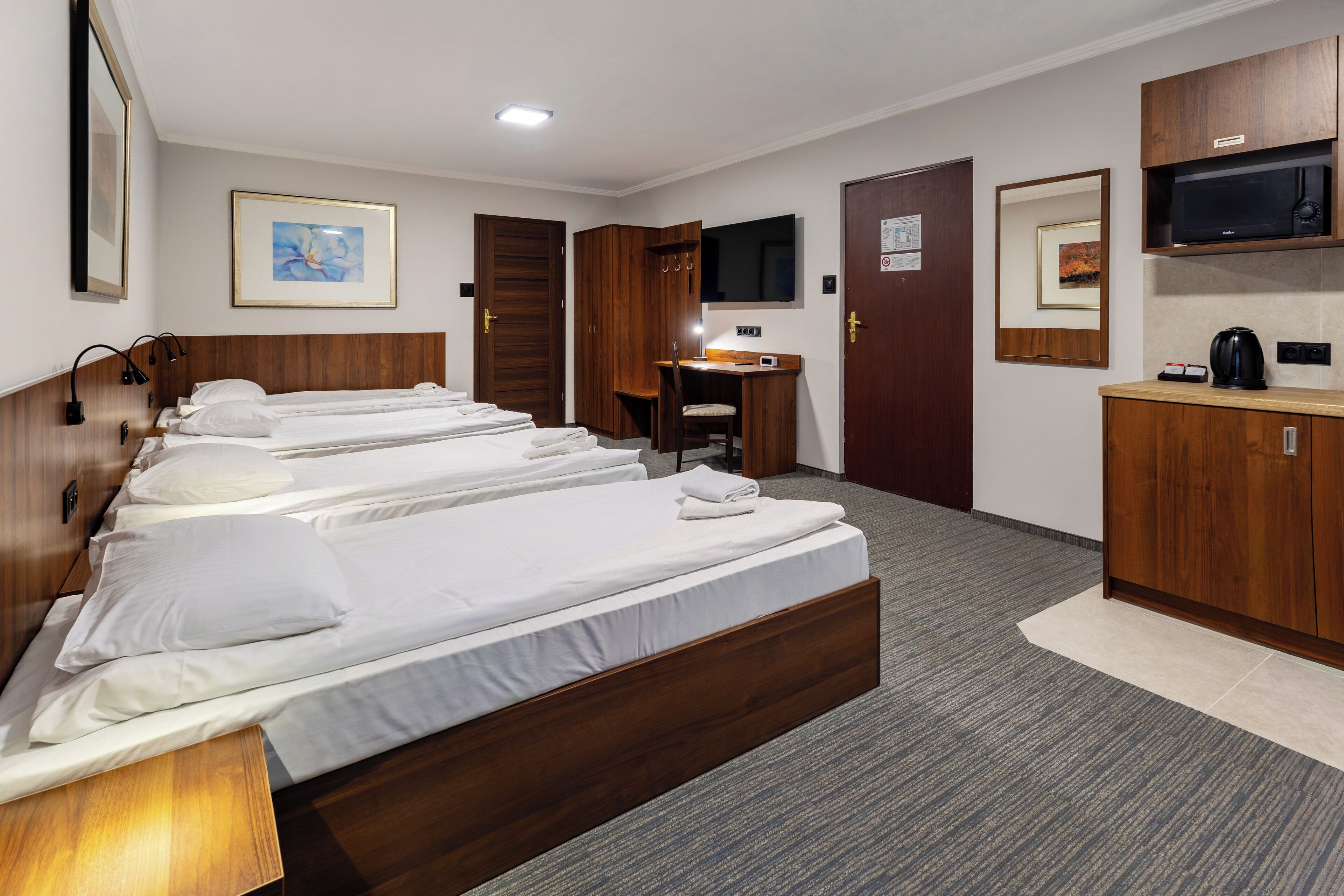 A hotel room with multiple beds, a desk, a television, and a microwave.