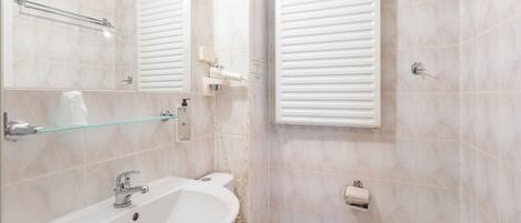 A bathroom with a white sink, toilet, and a glass shelf above the sink.