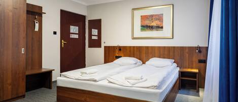 Habitación de hotel con cama de madera, dos almohadas, mesita de noche, armario y un cuadro en la pared.