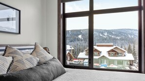 A bedroom with a large window, a bed with striped pillows, and a framed picture on the wall. - Switchback Creek Townhouse 17 (Sun Peaks)