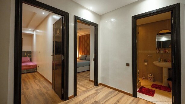A hallway with wooden flooring leading to a bedroom with a bed and a bathroom with a sink and toilet. - Luxury & Comfort apartment in the center, close to all amenities (Marrakesh)