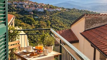 Ein Balkon mit Frühstückstisch, mit Blick auf ein Hügeldorf und Berge.