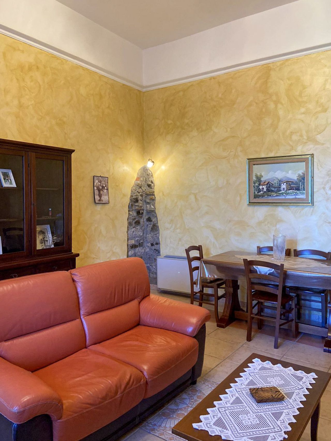 Een woonkamer met een leren bank, een eettafel met stoelen, een stenen zuil en een ingelijste foto aan de muur.