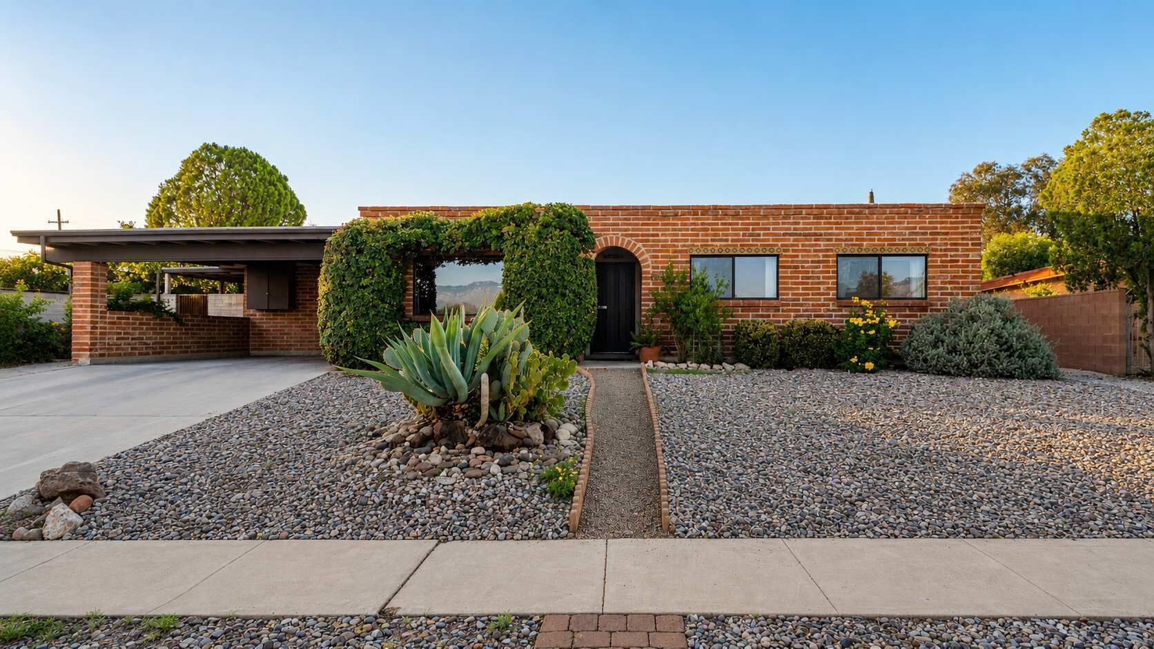 A modern brick house with a covered entryway, a gravel driveway, and a small garden with succulents.