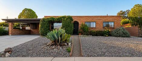 A modern brick house with a covered entryway, a gravel driveway, and a small garden with succulents.