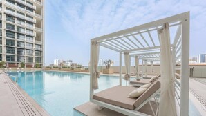 A rooftop pool area with a swing chair and lounge chairs, surrounded by a high-rise building. - StayShort - Sophisticated JVC Apartment Sleeps 4 with Balcony (JVC)