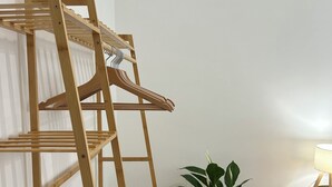 Ett träställ med flera våningar för att torka kläder, med kläder hängande på det, en krukväxt och en lampa placerade på ett trägolv.