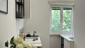 Ett modernt kök med ett fönster, vita skåp, en kaffebryggare och en vas med blommor på bänkskivan.