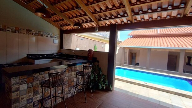 A kitchen with a tiled backsplash, a bar area with stools, and a view of a swimming pool. - Vacation home in Pirenópolis (Pirenópolis)