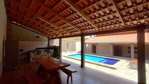 A covered outdoor area with a pool, wooden table, and kitchen area. - Vacation home in Pirenópolis (Pirenópolis)