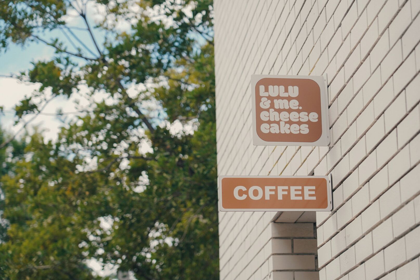 Two signs on a building wall: one reads "Lulu & me. cheese cakes" and the other "COFFEE".