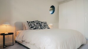 Quarto com cama, duas luminárias de cabeceira, um espelho redondo e um guarda-roupa.