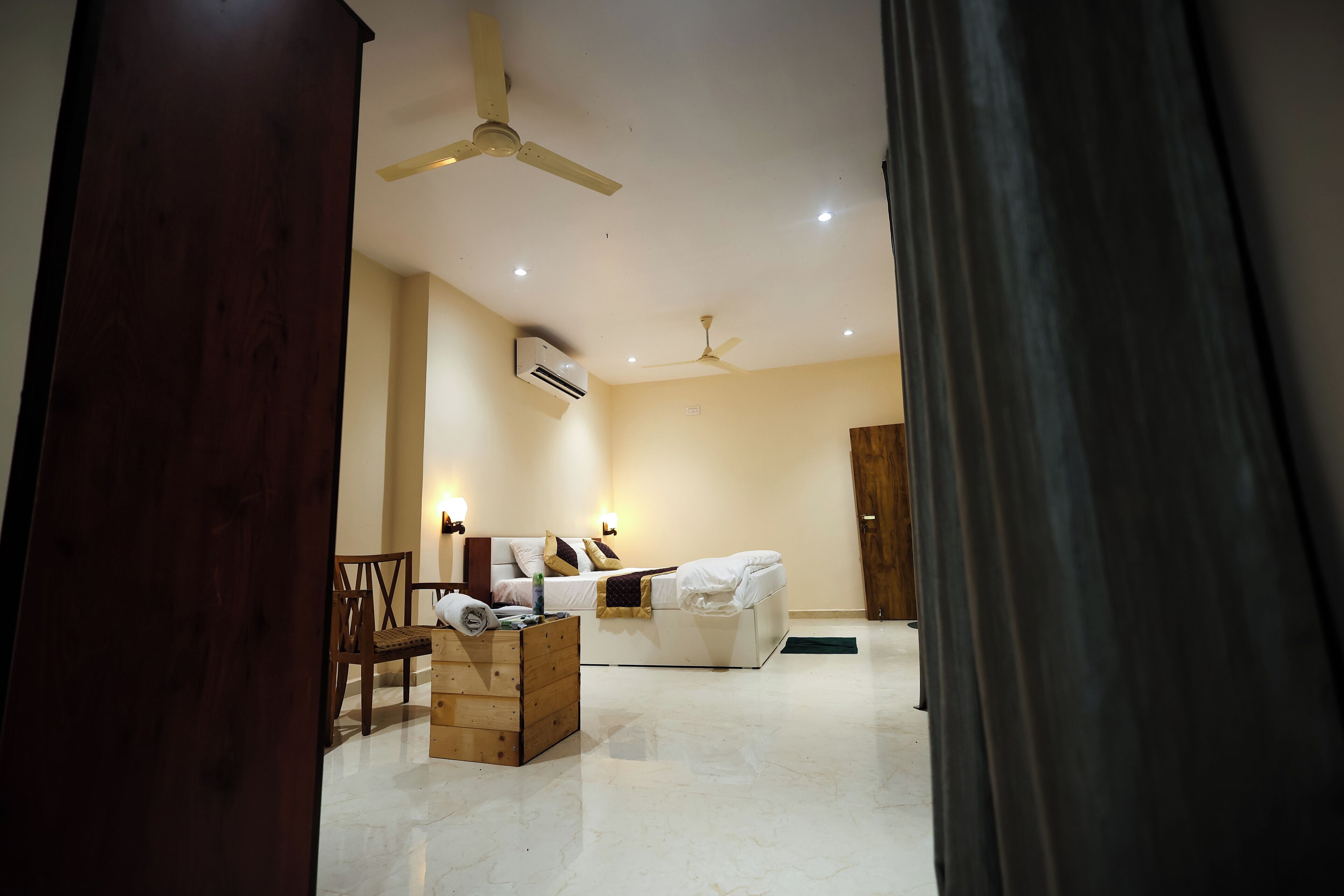 A hotel room with a bed, a wooden chest of drawers, a chair, and a ceiling fan.