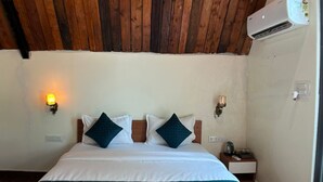 A bedroom with a wooden ceiling, a bed with white and teal bedding, two wall-mounted lamps, and a nightstand with a lamp and a cup. - A1 Tiger Resort (Chimur)