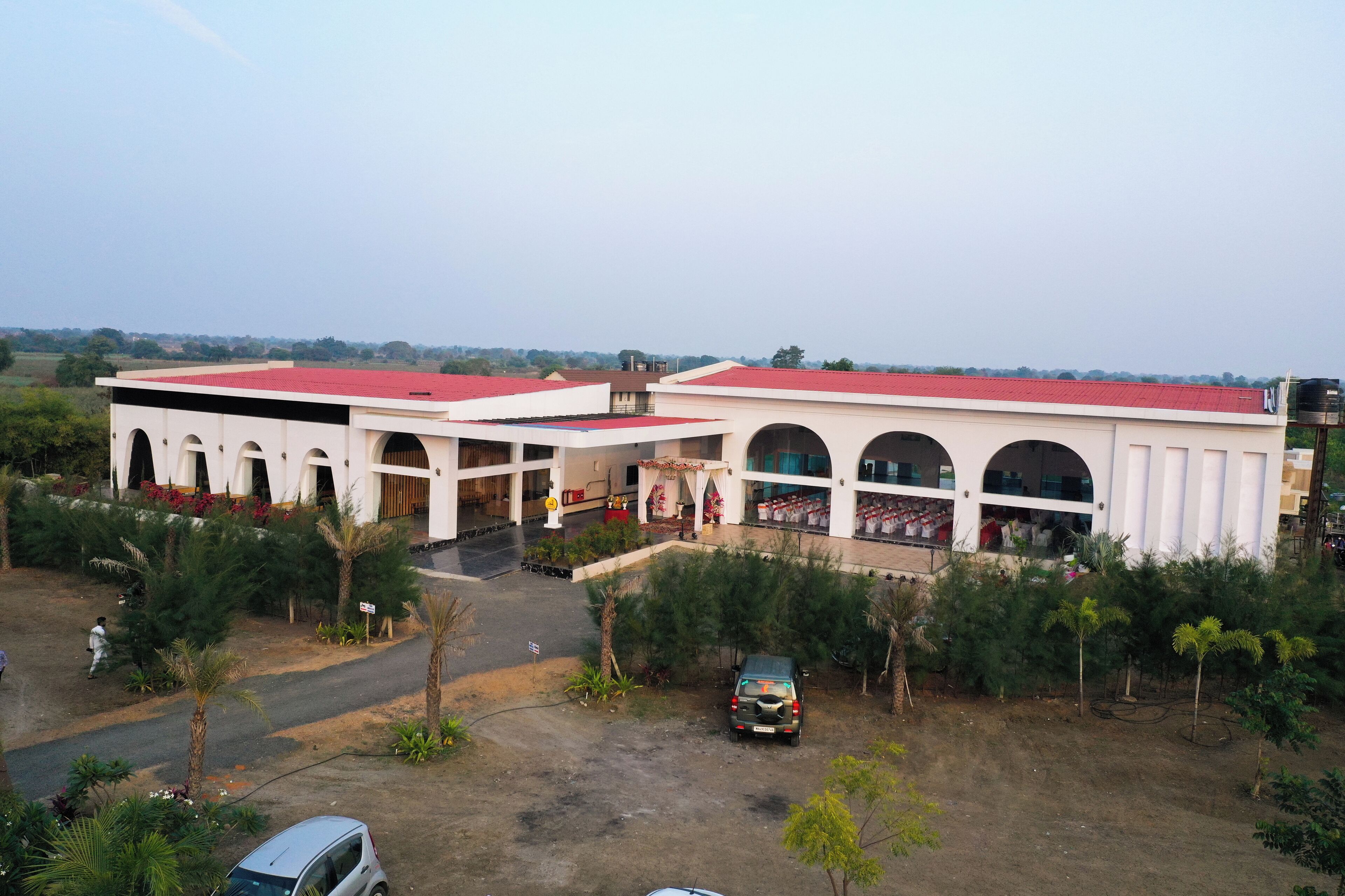 A building with multiple arched entrances, a red roof, and a parking area with a few vehicles.