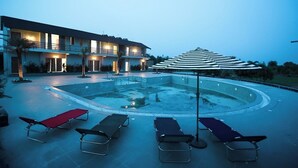 A hotel with a swimming pool, lounge chairs, and a covered area with umbrellas. - A1 Tiger Resort (Chimur)