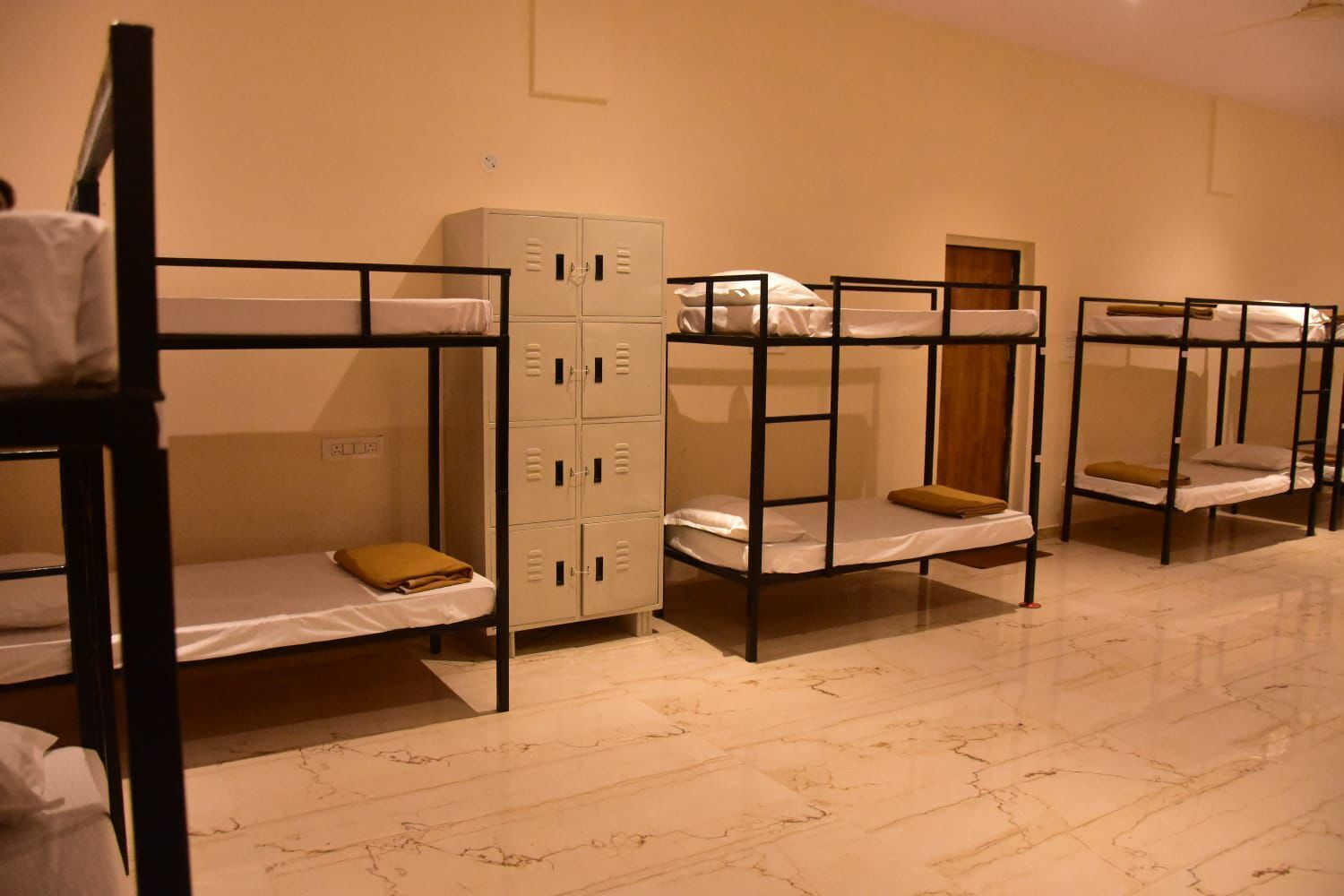 A dormitory room with bunk beds, a wardrobe, and a door.