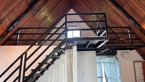 A spacious attic room with a wooden floor, a metal staircase, and a loft area with a window. - A1 Tiger Resort (Chimur)