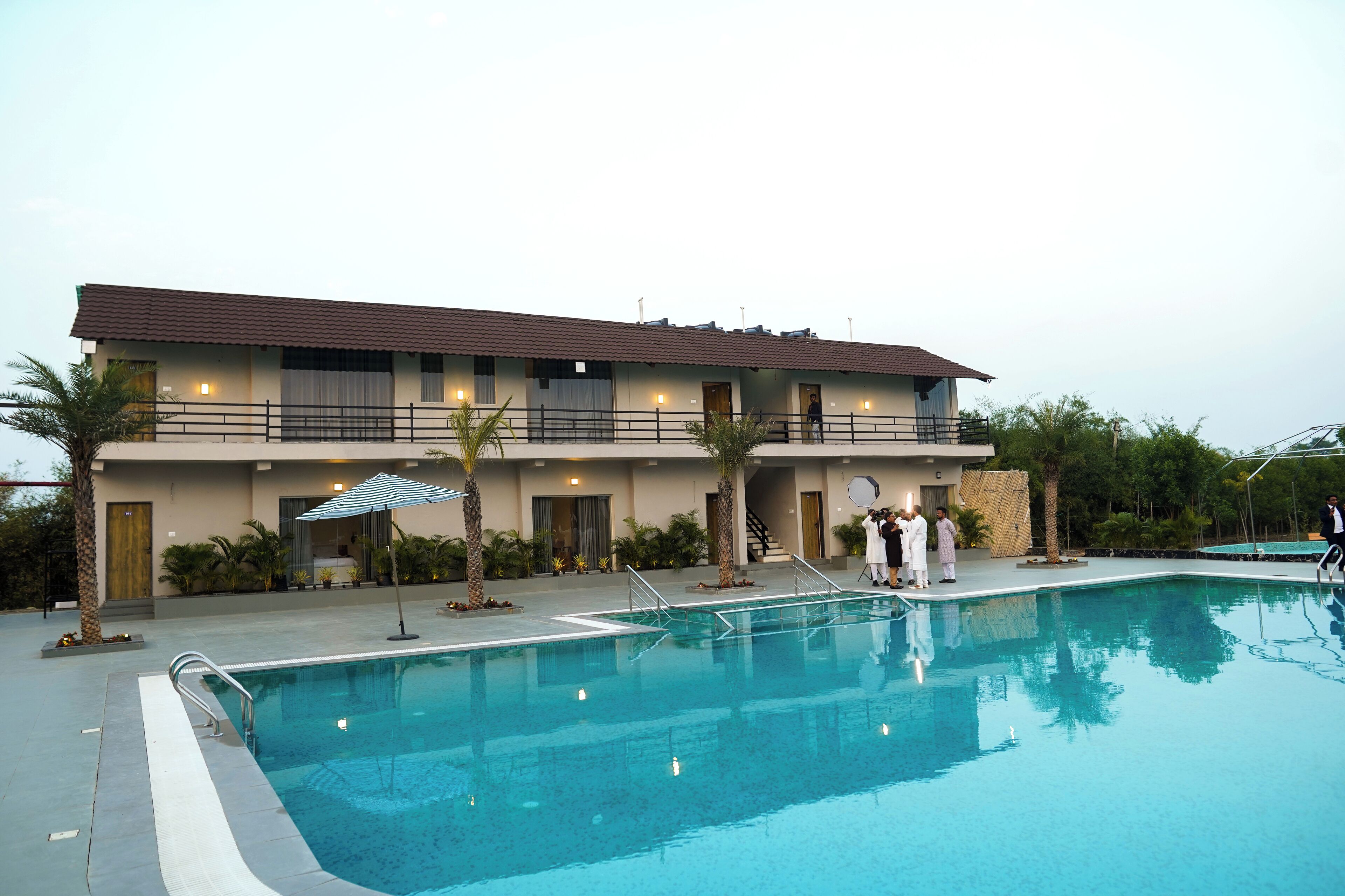 Un hotel de dos pisos con piscina, un patio cubierto y un jardín ajardinado.
