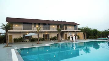 Un hotel de dos pisos con piscina, un patio cubierto y un jardín ajardinado.