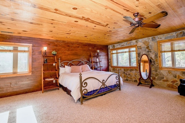 Un dormitorio con techo de madera, una cama con estructura metálica, pared de piedra y un espejo grande.