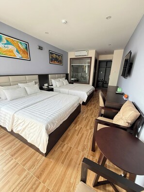 A hotel room with two beds, a dining table, a chair, a TV, and artwork on the walls. - Novelty Hotel (Ho Chi Minh City)
