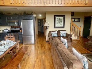 A living room with a brown sofa, a dining table with chairs, a kitchen with appliances, and a staircase. - Peekin'Over Pigeon Forge 3 bedroom, 3 bath cabin (Sevierville)