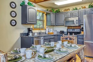 A kitchen with grey cabinets, a microwave, and a dining table set with plates and cups. - Peekin'Over Pigeon Forge 3 bedroom, 3 bath cabin (Sevierville)
