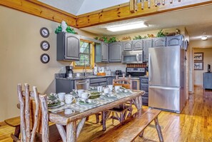 A kitchen with wooden cabinets, a stainless steel refrigerator, and a dining table set with white dishes. - Peekin'Over Pigeon Forge 3 bedroom, 3 bath cabin (Sevierville)