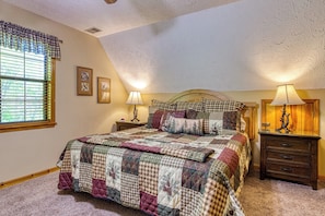 A bedroom with a large bed, two bedside tables with lamps, a window with blinds, and a ceiling with a textured finish. - Peekin'Over Pigeon Forge 3 bedroom, 3 bath cabin (Sevierville)