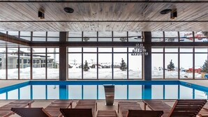 An indoor swimming pool with wooden loungers and large windows overlooking a snowy landscape. - New Gudauri Cozy Studio By Wehost (Gudauri)