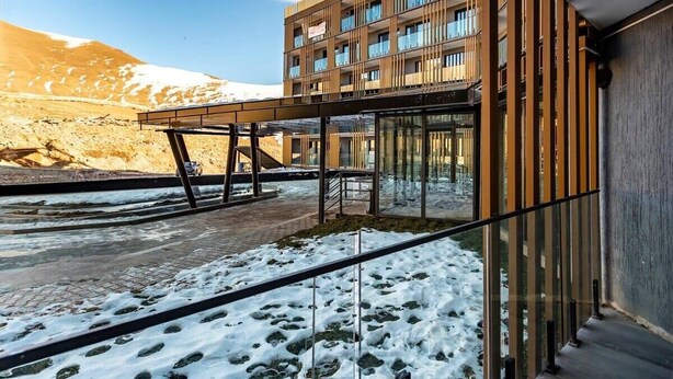 A modern building with a glass facade, a wooden exterior, and a view of a snowy landscape. - New Gudauri Cozy Studio By Wehost (Gudauri)
