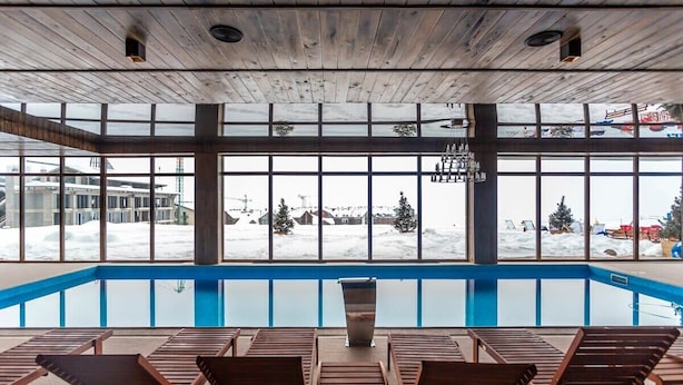 An indoor swimming pool with wooden loungers and large windows overlooking a snowy landscape. - Studio near Gondola in New Gudauri by Wehost (Gudauri)