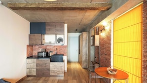 A compact kitchen with wooden cabinets, a microwave, and a sink. There is a dining area with a table and chairs, and a bean bag chair in the corner. - Studio near Gondola in New Gudauri by Wehost (Gudauri)