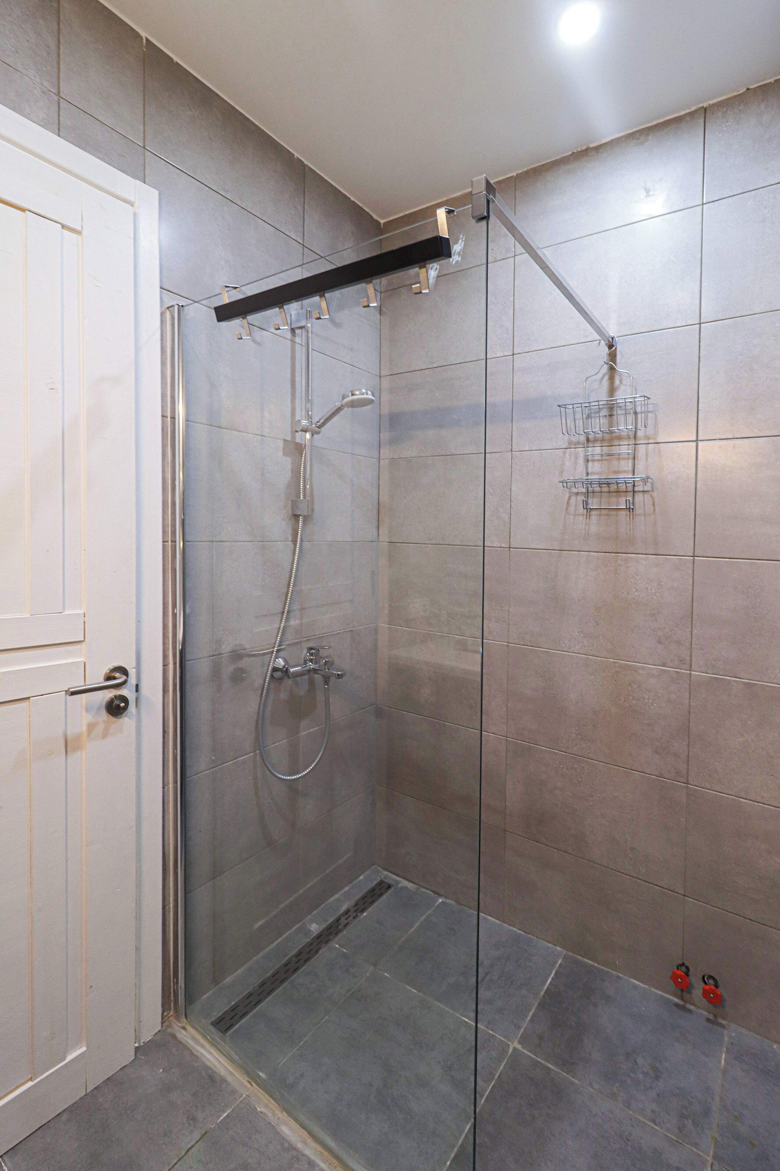 A glass-enclosed shower with a handheld showerhead and a wall-mounted faucet.