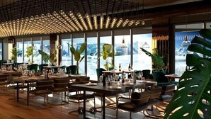 Ein Restaurant mit mehreren Tischen und Stühlen, großen Fenstern mit Bergblick und hängenden Leuchten.