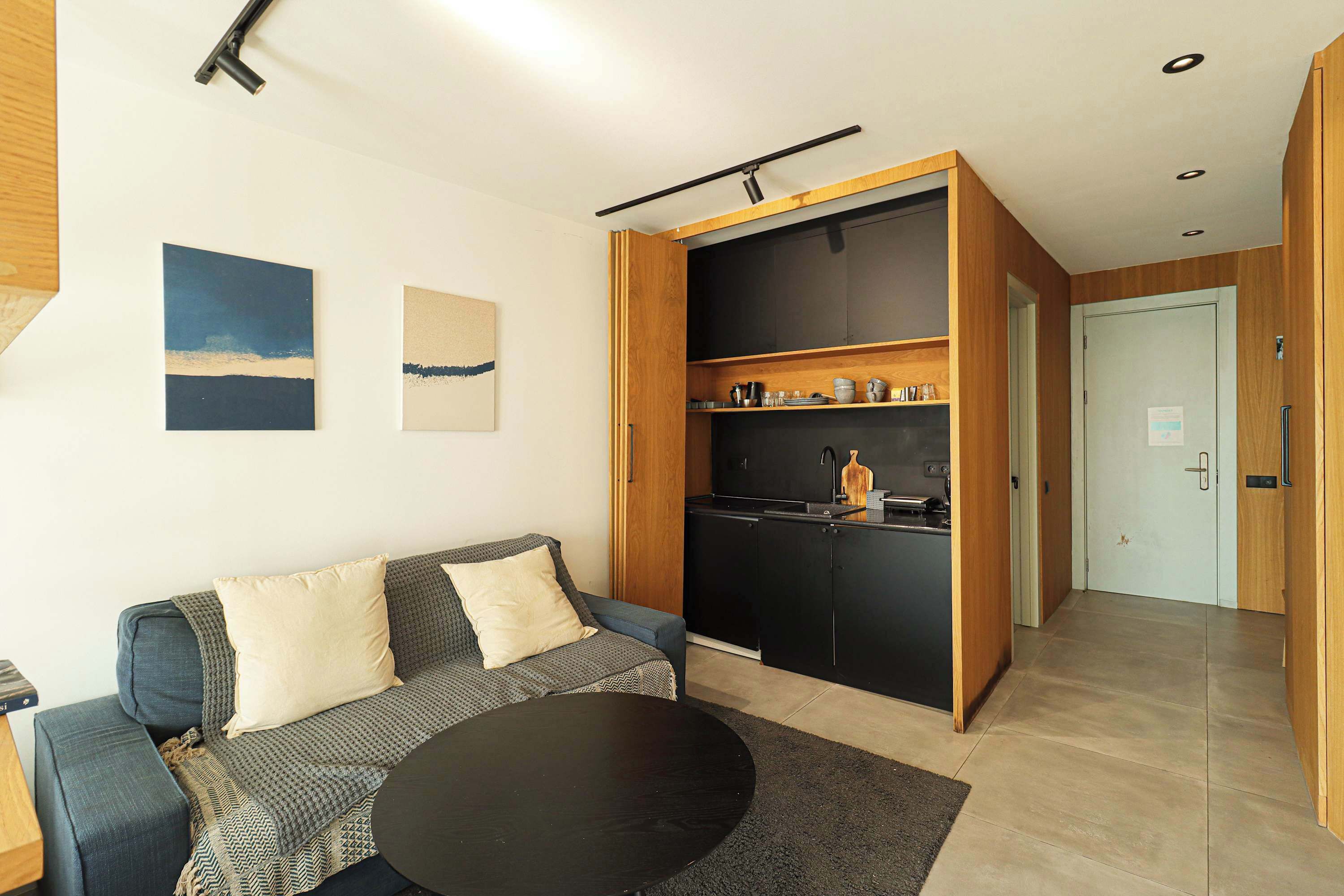 Una sala de estar moderna con sofá, una mesa de centro y una zona de cocina con armarios y electrodomésticos.
