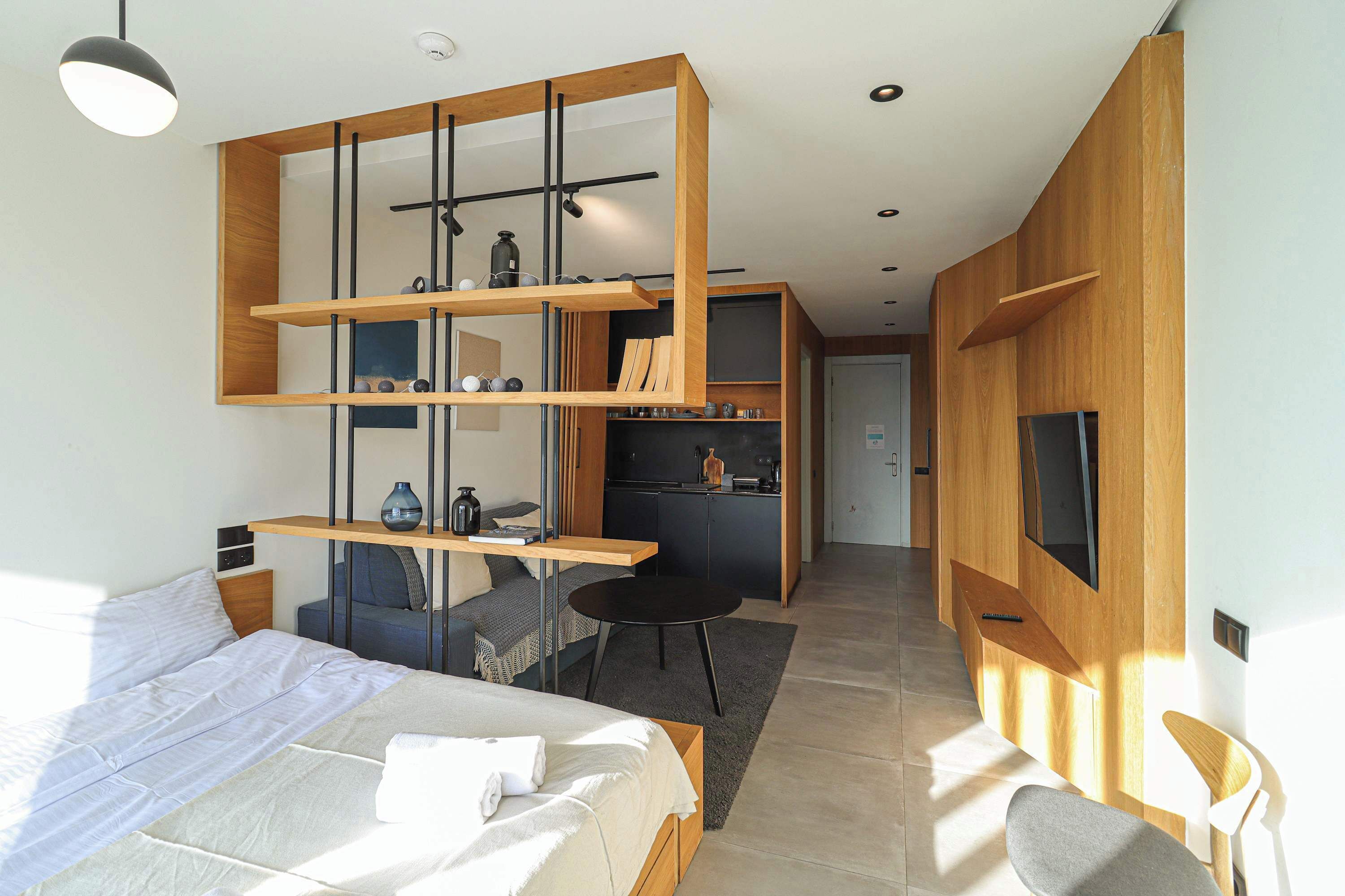 A modern bedroom with a bed, a desk, and a kitchenette.