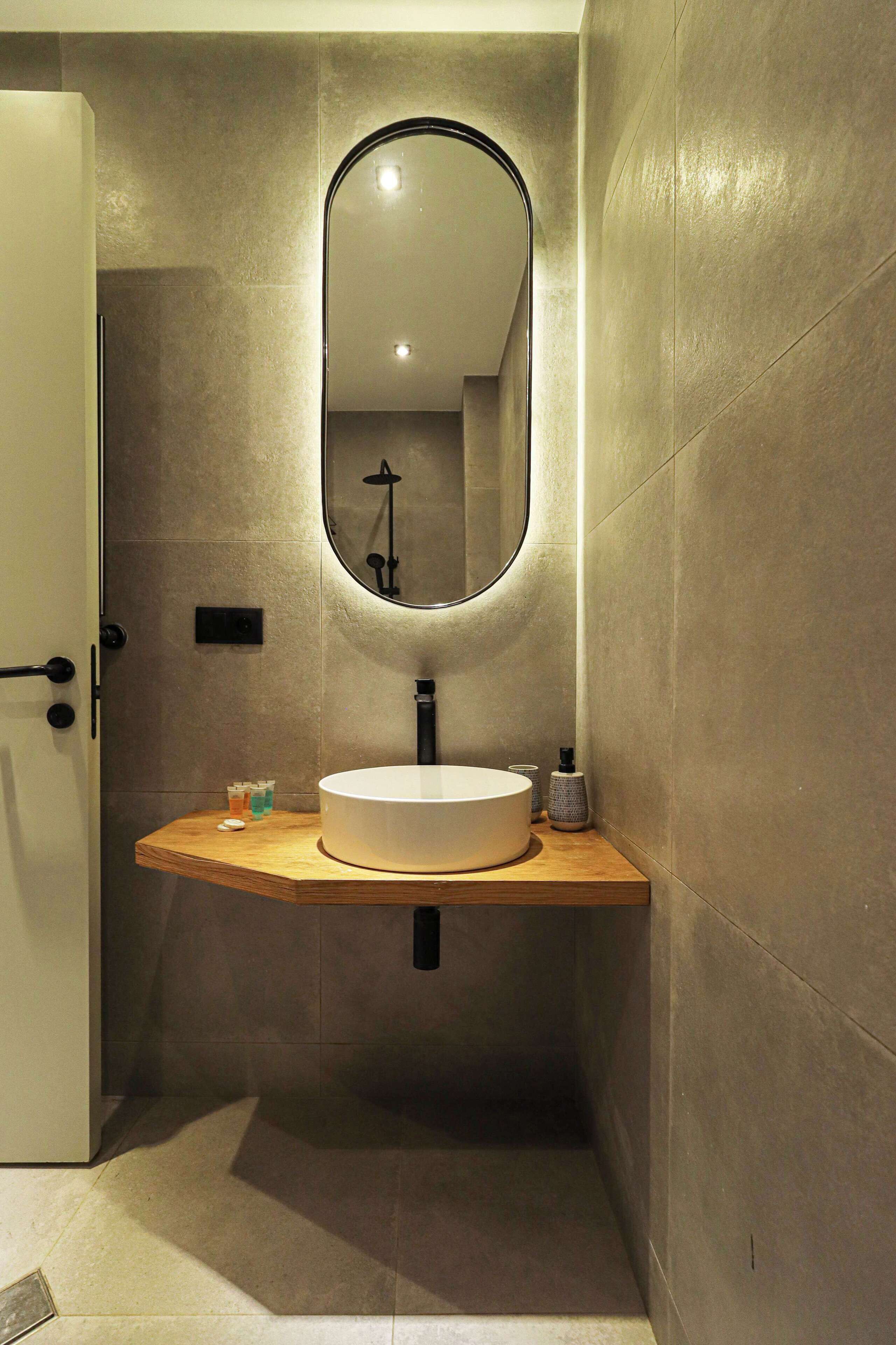 Ein modernes Badezimmer mit rundem Spiegel, Waschtisch aus Holz und weißem Waschbecken.