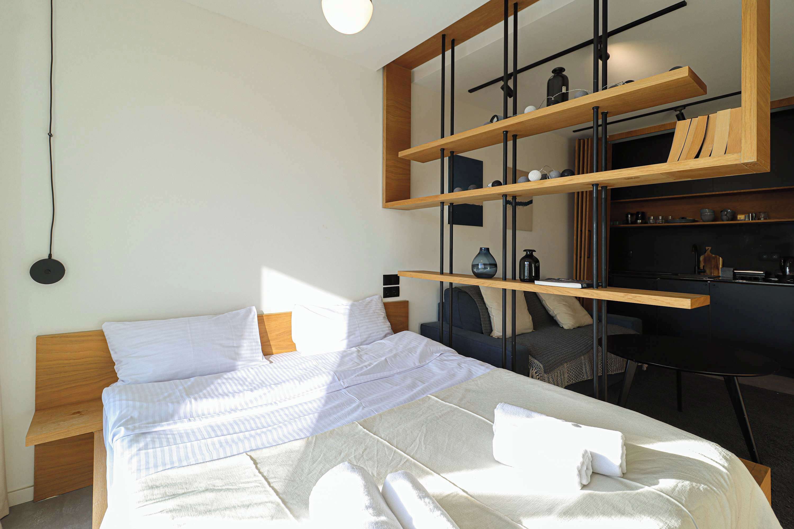 Une chambre d’hôtel moderne avec un lit soigneusement fait, un bureau avec une chaise et des étagères intégrées au-dessus du bureau.