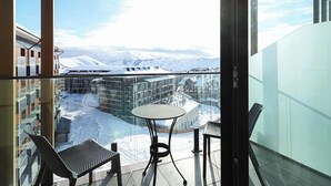 Ein Balkon mit Tisch und zwei Stühlen, mit Blick auf eine verschneite Landschaft mit Gebäuden und Bergen.