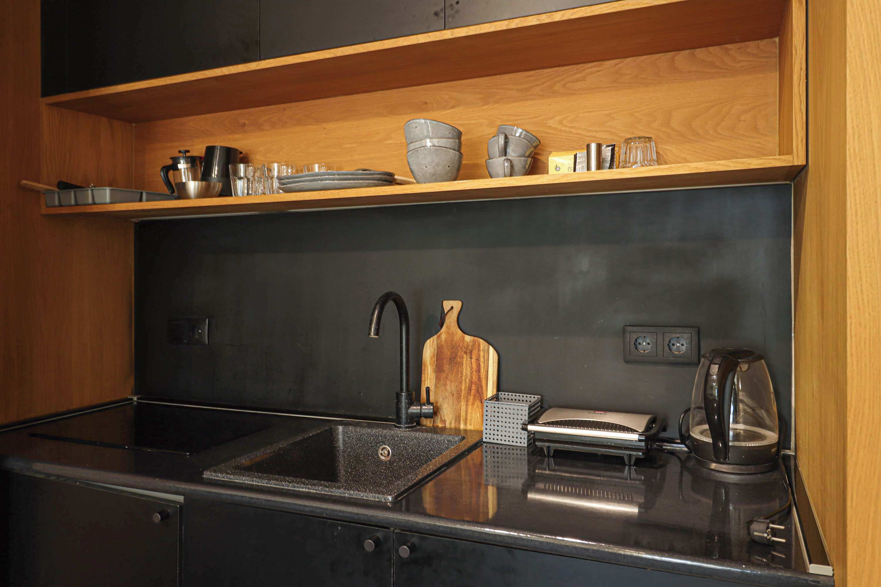A modern kitchen with a black sink, stainless steel appliances, wooden shelves, and a coffee maker.