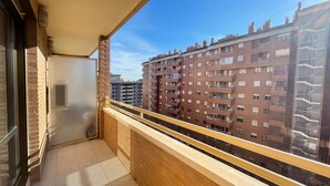 A balcony with a view of high-rise buildings, a tiled floor, and a wooden railing. - Apartamentos el Pilar Suites 3000 (Zaragoza)