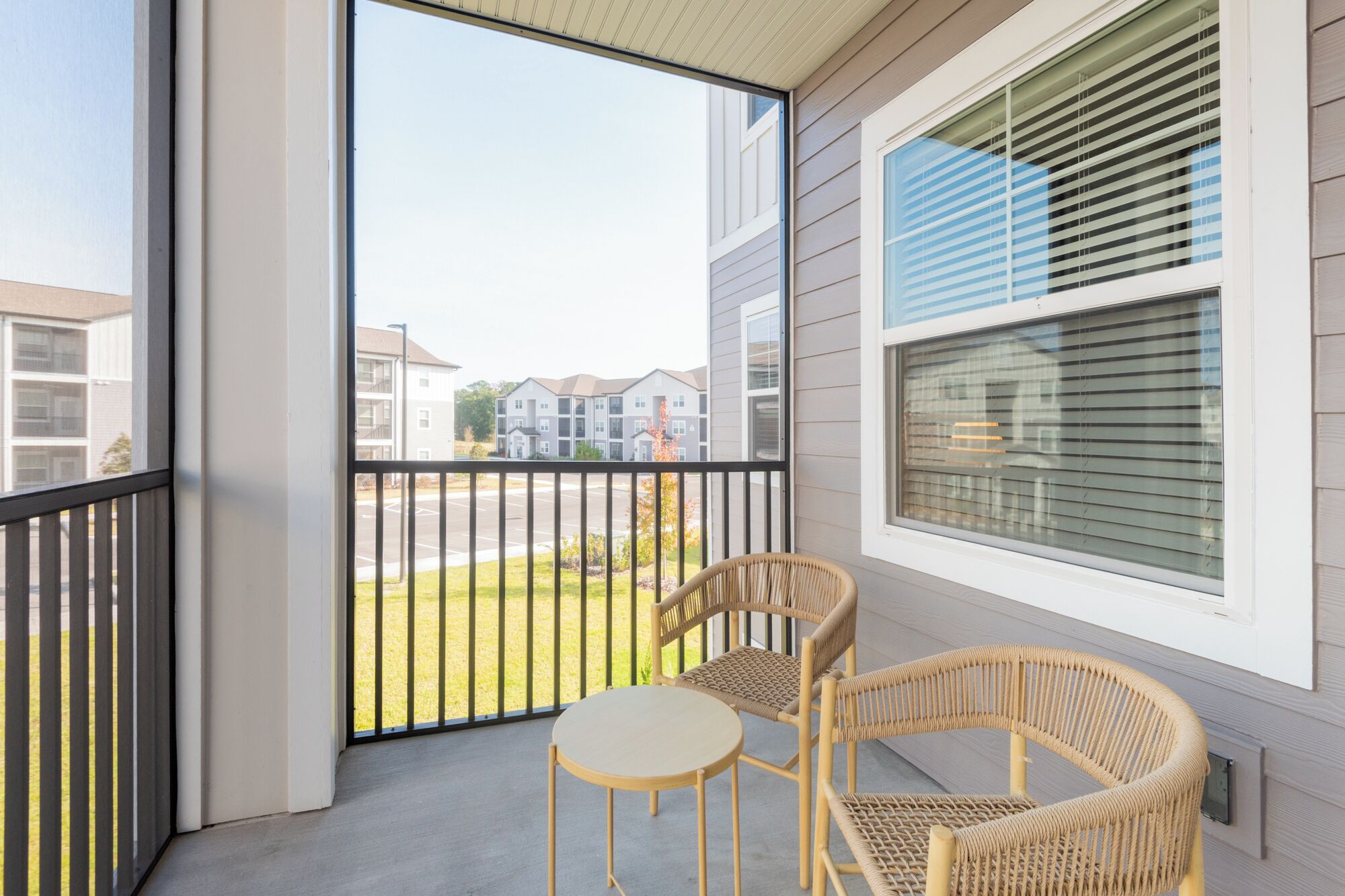 A balcony with two wicker chairs and a small round table, overlooking a residential area.