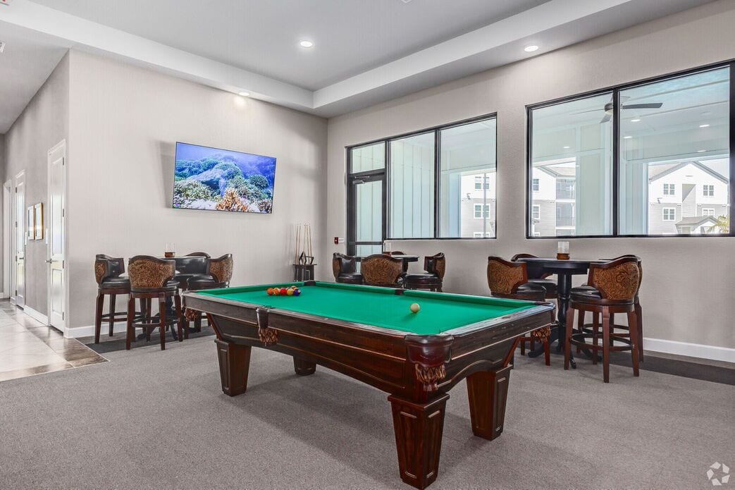A pool table in a room with large windows, chairs, and a painting on the wall.