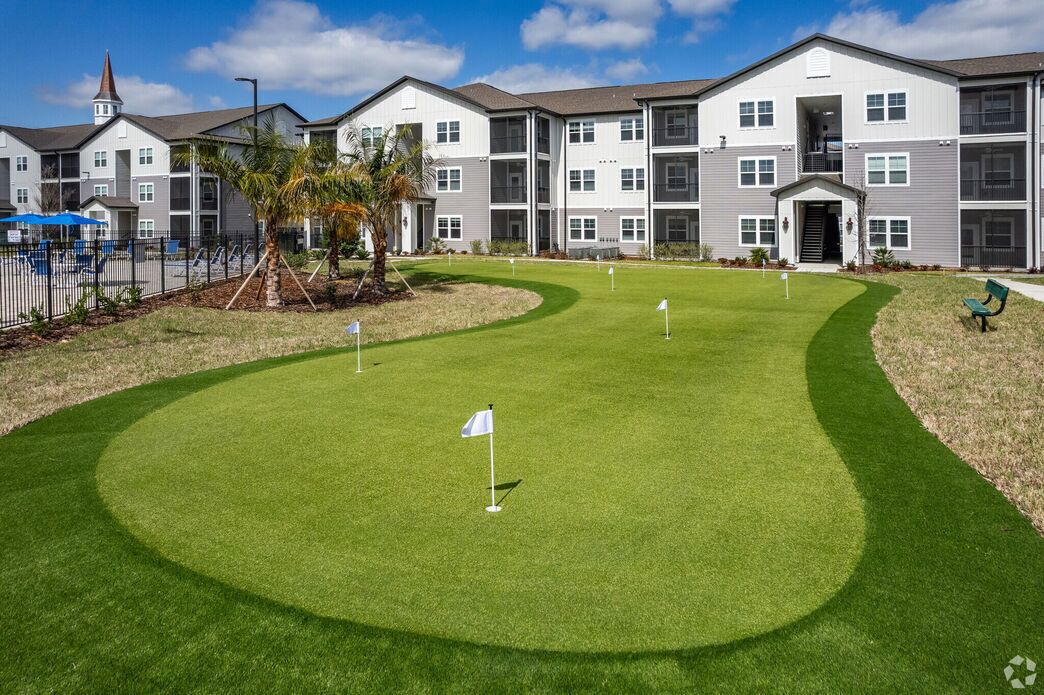 A well-maintained golf course with a clear flag, surrounded by a multi-story residential building with a modern architectural style.