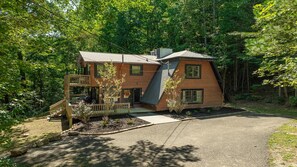 A two-story wooden cabin with a balcony, surrounded by a forest. - Sugar Bear Cabin- 4bdrm, Semi-Private, Fire-pit, Hot Tub, and Tranquil setting (Pigeon Forge)