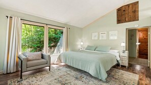 A bedroom with a bed, a chair, a nightstand, a lamp, and a window with curtains. - Sugar Bear Cabin- 4bdrm, Semi-Private, Fire-pit, Hot Tub, and Tranquil setting (Pigeon Forge)