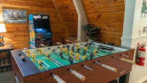 A foosball table in a room with wooden walls and a mounted arcade game. - Sugar Bear Cabin- 4bdrm, Semi-Private, Fire-pit, Hot Tub, and Tranquil setting (Pigeon Forge)