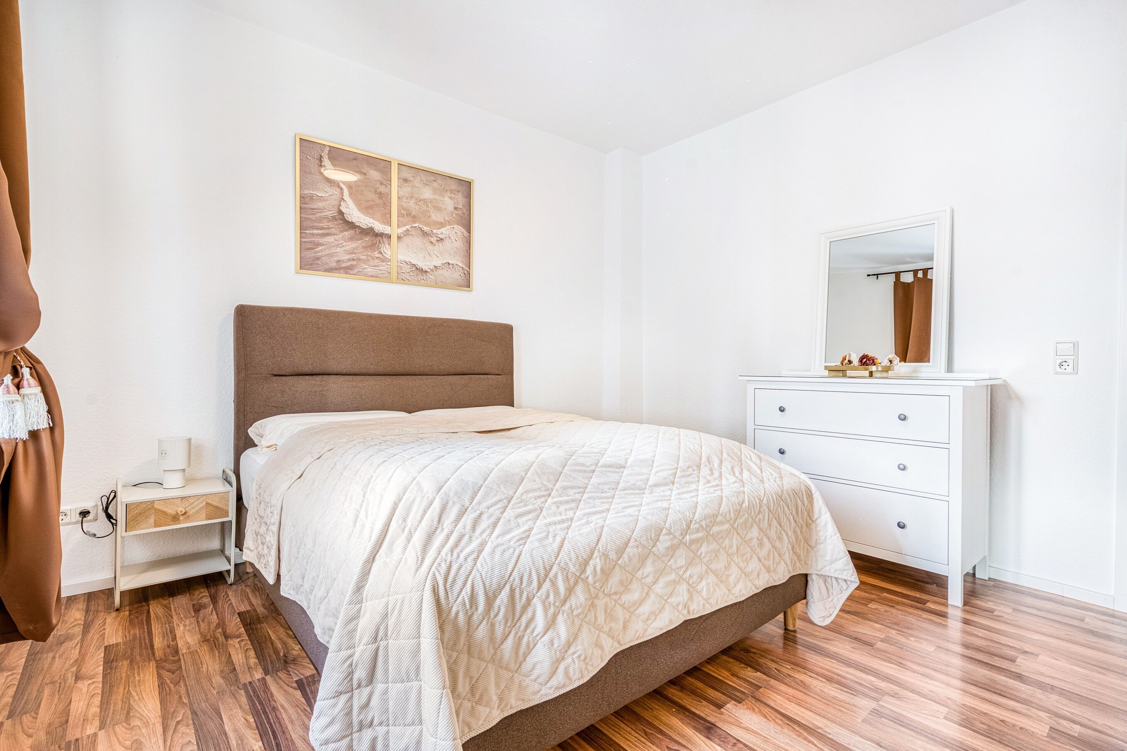 Un dormitorio con cama, mesita de noche, cómoda y un cuadro colgado en la pared.